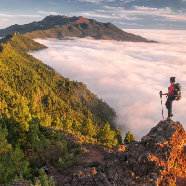 Sendero en la cumbre de La Palma al atardecer, con el mar de nubes y una senderista sobre las rocas