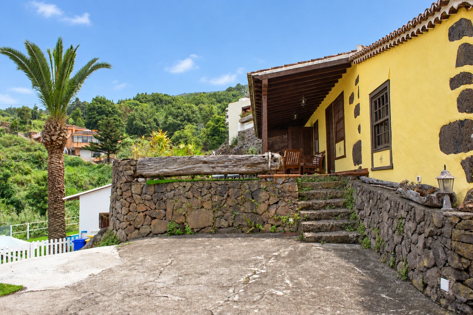 La fachada amarilla de Cha Miquela Pequeña, con la palmera y el muro de piedra