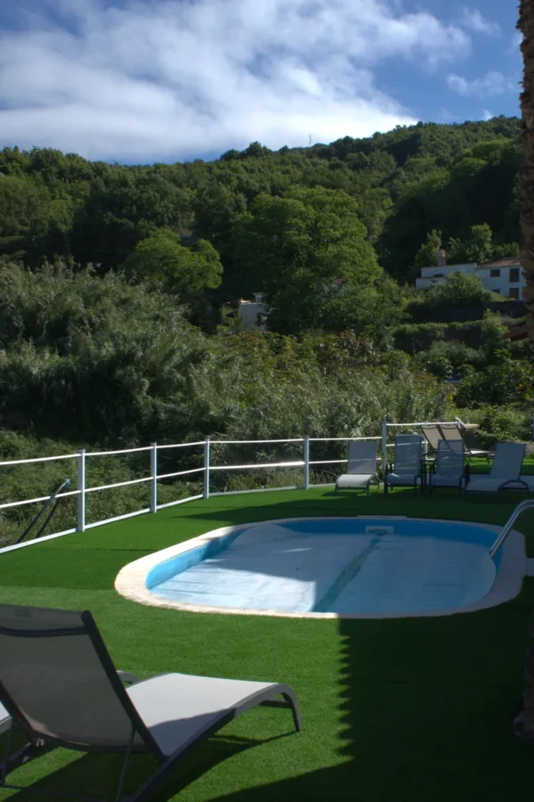 La piscina compartida de Cha Miquela, con el césped, las tumbonas y la ladera de la laurisilva detrás